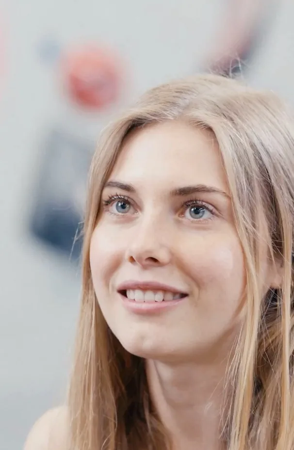 Hannah Meul zwischen zwei Einstellungen Hannah Meul zwischen zwei Einstellungen des Videos: sie lächelt und sieht an der Kamera vorbei, hinter ihr unscharf die Griffe der Boulderhalle