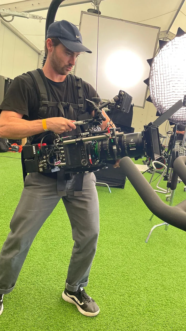 Kameramann am Körperstativ — Social Ad Produktion Kameramann mit Körperstativ und ARRI-Kamera geht am Spinning-Rad entlang, dahinter eine große Rundleuchte