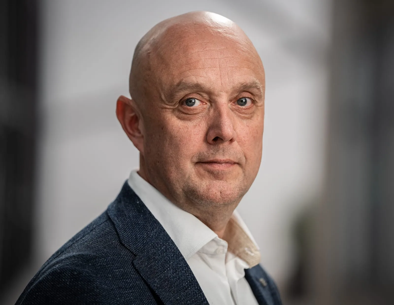 Unternehmensporträt vor hellem Hintergrund Unternehmensporträt vor hellem Hintergrund: Mann mit kahlem Kopf im blau melierten Sakko, leicht zur Seite gedreht