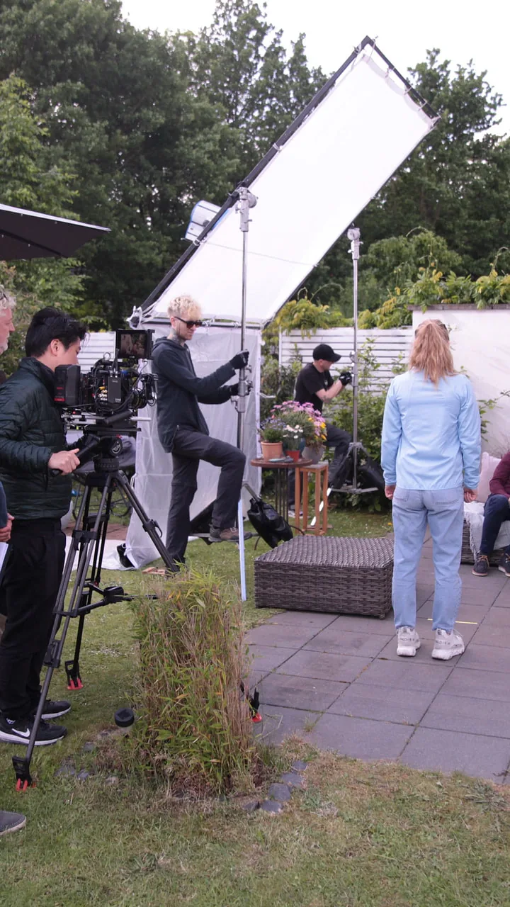 Aufbau im Garten für Video und Produktfotografie: Crew, Stative und ein großer Diffusor vor einer Terrasse, rechts die Moderatorin