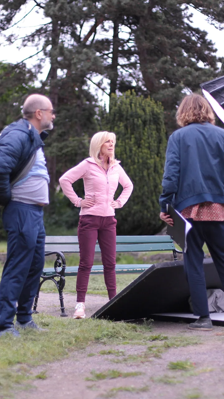Die Moderatorin im Park zwischen Kamera und Reflektor, links und rechts die Crew