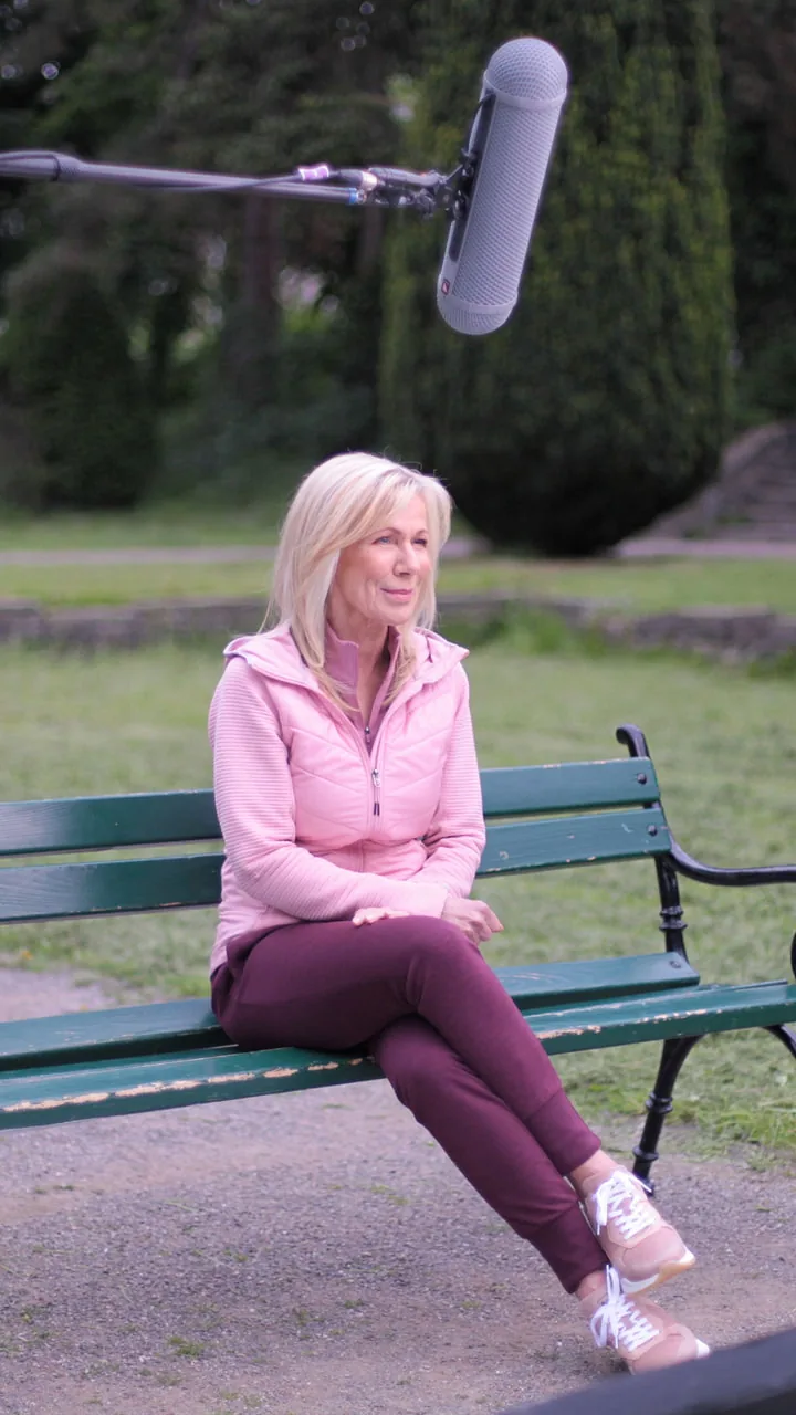 Tonangel über der Parkbank beim Dreh des TV-Spots: Ulrike von der Groeben sitzt in rosa Jacke auf einer grünen Parkbank