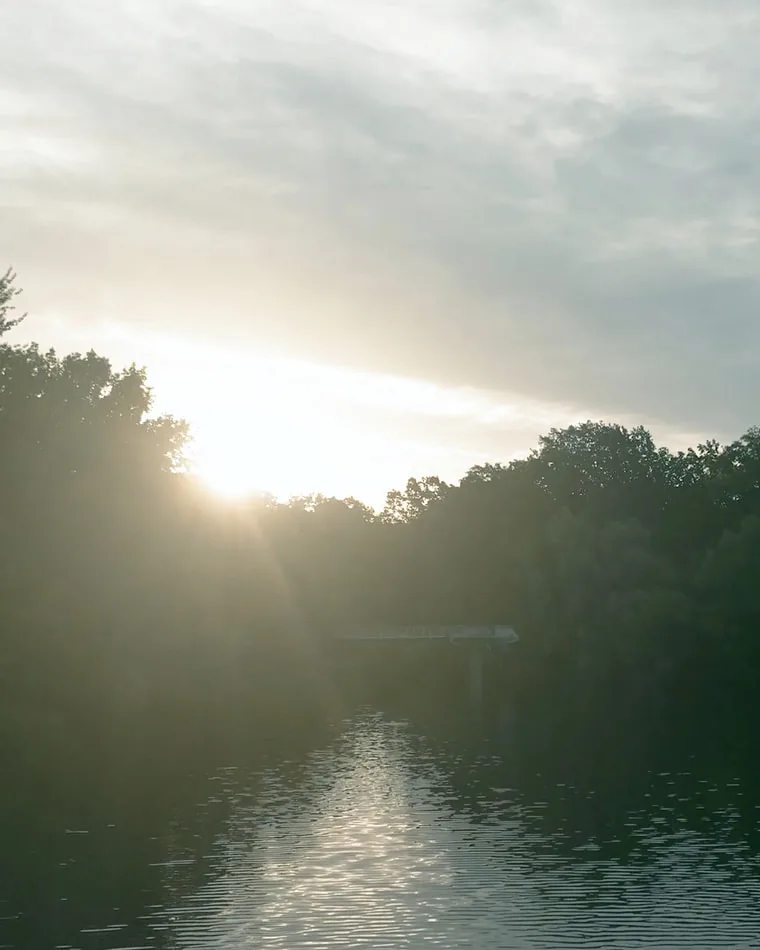 Abendstimmung am See aus dem Porträtfilm Die tiefstehende Sonne über einem See, links und rechts die dunkle Baumkante, am Ufer ein schmaler Steg