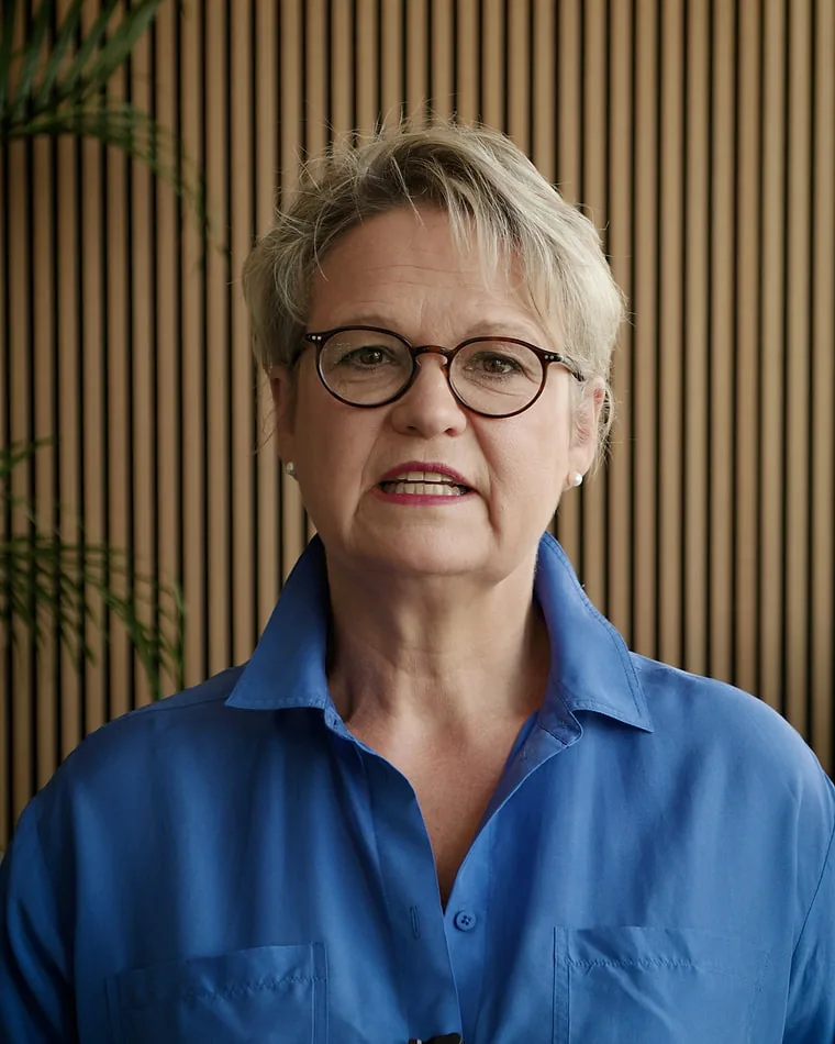Interview vor der Kamera — Social Media Kampagne für Siemens Interviewaufnahme für das Mitarbeiterporträt: Frau mit Brille im blauen Hemd spricht in die Kamera, hinter ihr eine Holzlamellenwand, links ein Farn