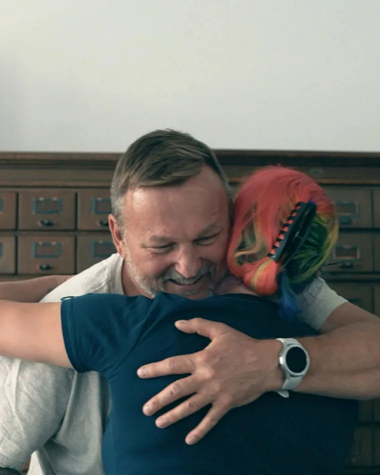 Lydia mit einem Kollegen — Mitarbeiterporträt für Siemens Aus dem Video für Siemens: ein Kollege nimmt Lydia lachend in den Arm, dahinter eine Wand aus alten Holzschubladen
