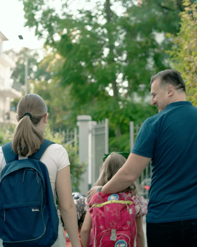 Vedad mit seiner Familie — Porträtfilm für Siemens Vedad geht mit seiner Familie eine Allee hinunter, von hinten gesehen, die Kinder mit Schulranzen
