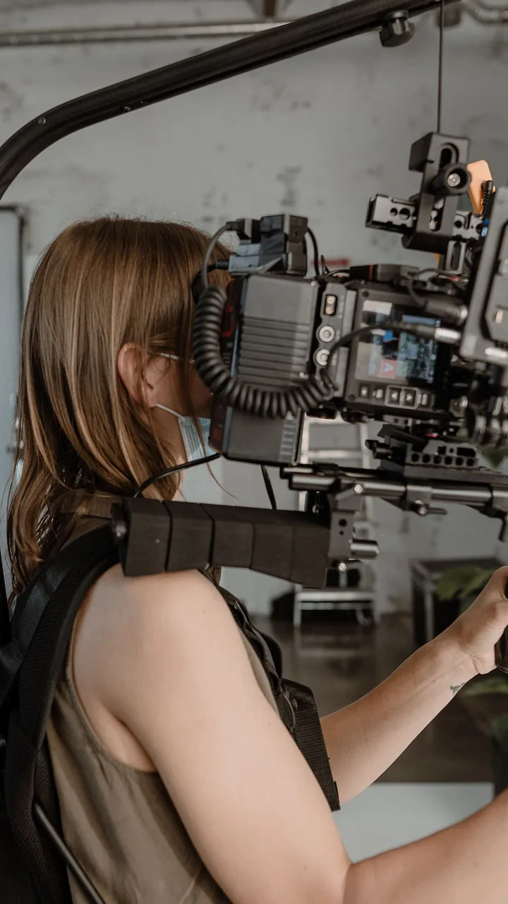 Camerawoman in a face mask on a body rig, seen from the side, camera and transmitter at eye level