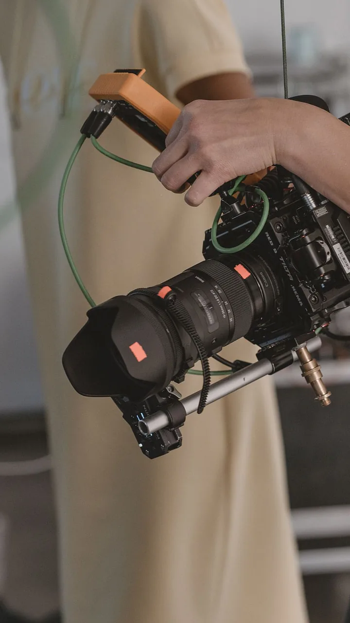 One hand on the orange grip of the camera rig, lens and matte box in front, a green cable running past