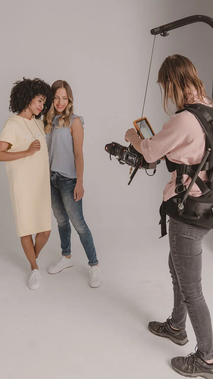 On the set of the social content production for Street One: two models against a pale backdrop, the camerawoman at right on a body rig with an orange monitor on an arm
