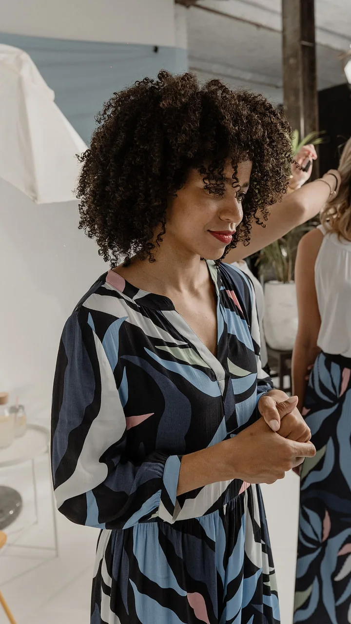 Model in a blue patterned dress looking to the side, the second model being styled behind her
