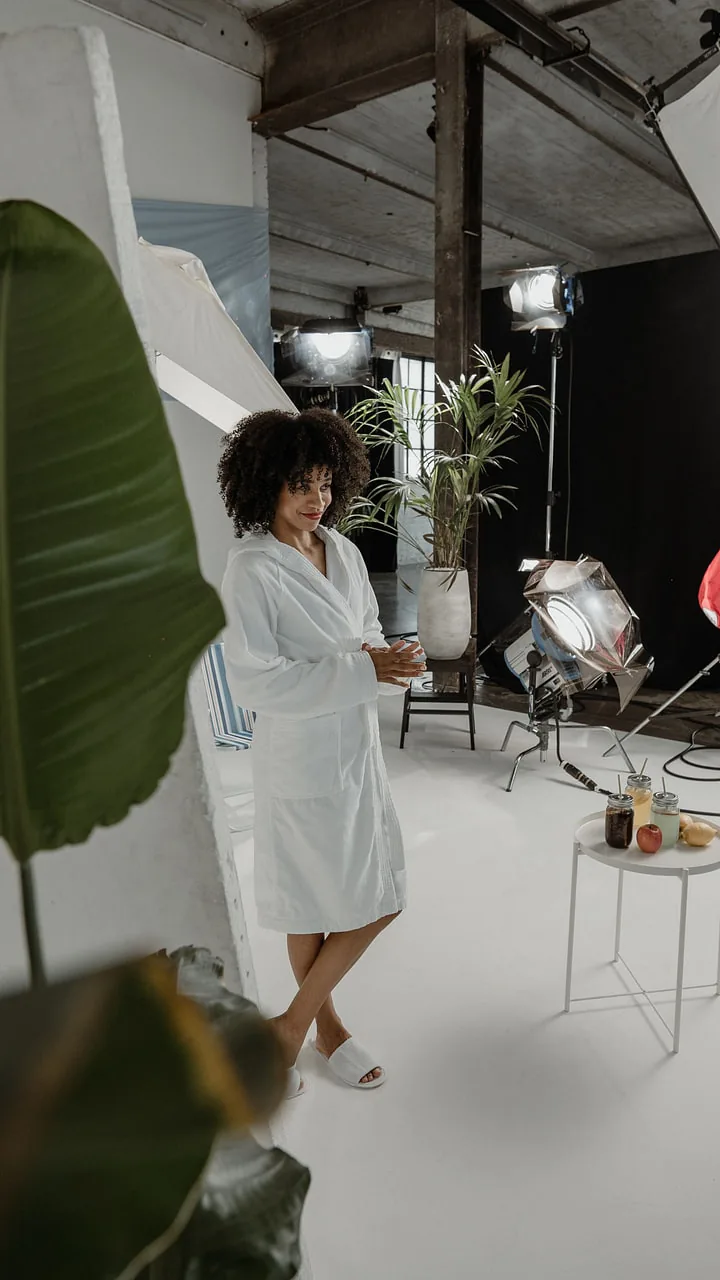 A model in a white bathrobe on the studio floor between plants and lights