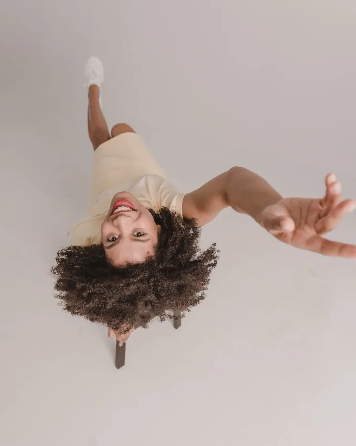 A movement shot for the Street One feed: model laughing upside down in frame, in a pale yellow top, arms stretched wide