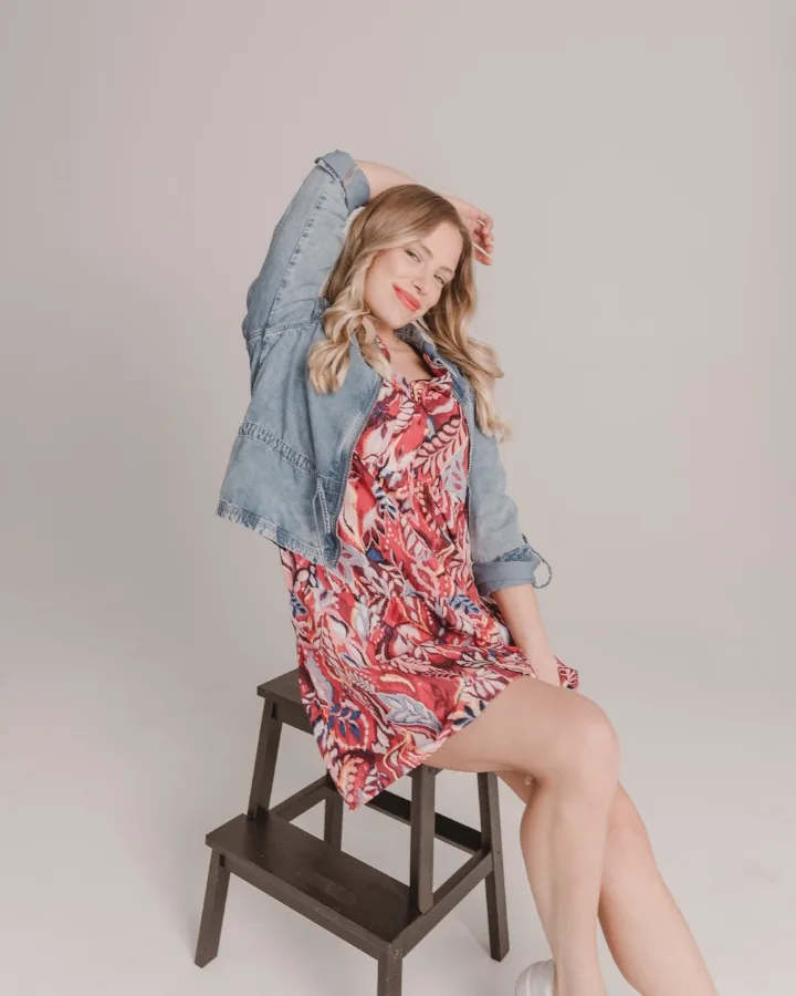 Campaign photo for Street One: model in a floral dress and denim jacket, sitting on a step stool against a pale backdrop