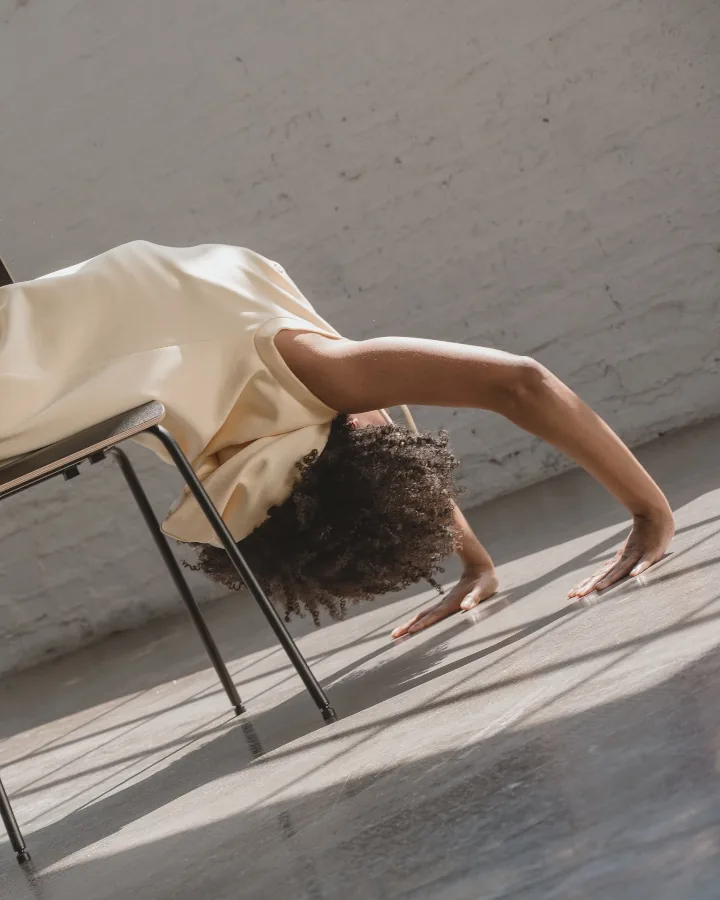 Model lying back over a chair, the cream dress backlit, one hand on the sunlit floor