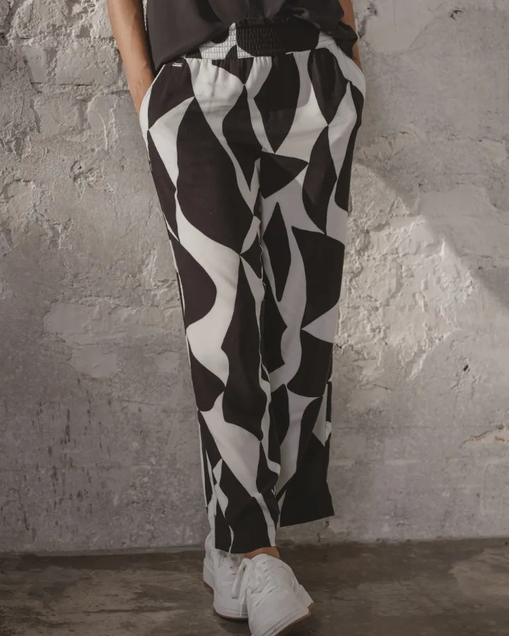 Model in black and white patterned trousers and a dark top by the rendered wall, hands in her pockets