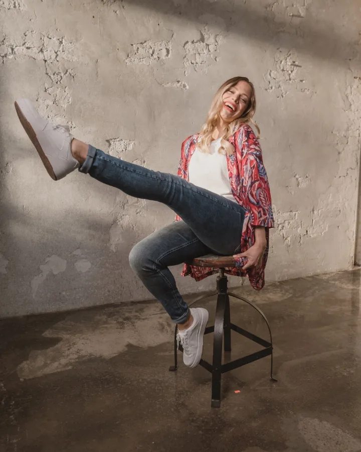 Model in jeans and a floral kimono on a stool, one leg kicked far out