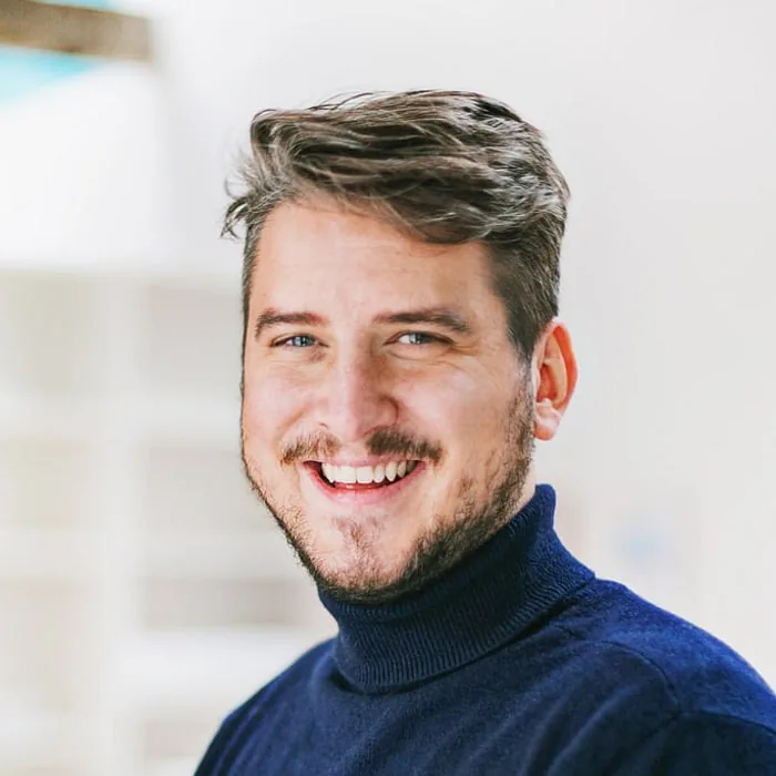 Philipp Maxhofer, creative director at Le Werk in Cologne, in a navy roll-neck, laughing in front of the bright studio shelving