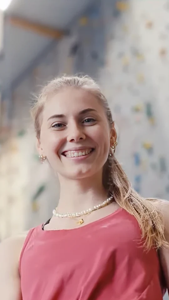 Still from the athlete portrait for Allianz × Olympia: climber Hannah Meul laughing into the camera, the colourful bouldering wall blurred behind her