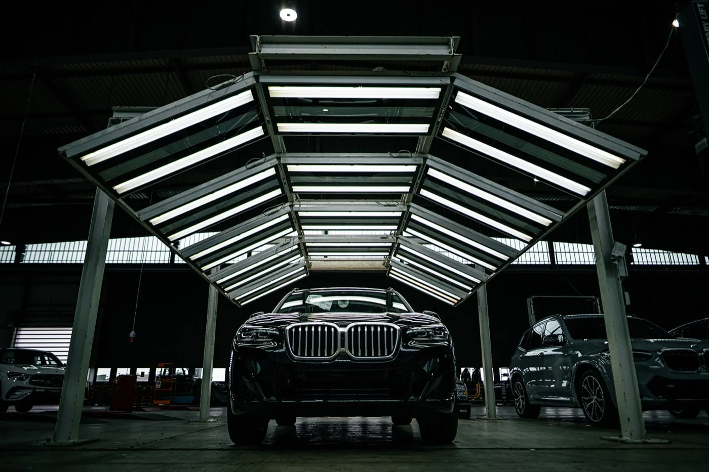 Corporate photography for Formel D: dark SUV head-on beneath an open canopy of fluorescent tubes in a workshop hall