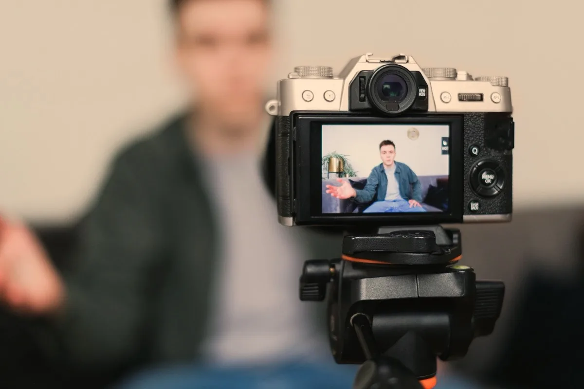 Recording during the workshop: speaking on camera A man speaking on camera, seen on its display — he himself stands out of focus behind the tripod