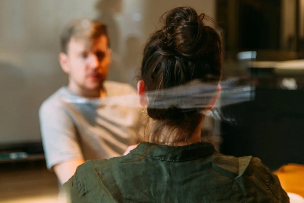 Conversation during the workshop Two people in conversation at a table, photographed from behind through a pane of glass