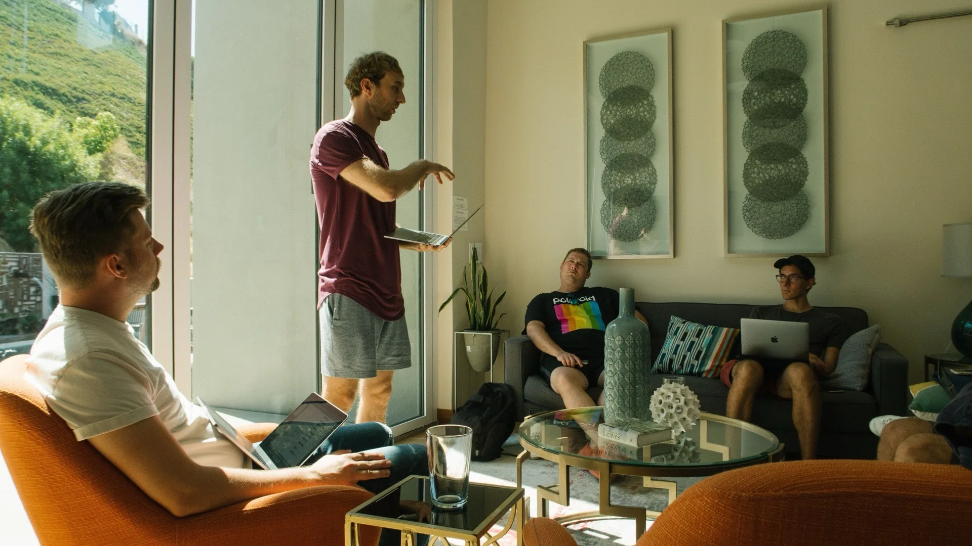 Improv workshop for teams and companies Improv workshop at a company: four men in a bright living room, one standing at the window explaining something, a tablet in his hand