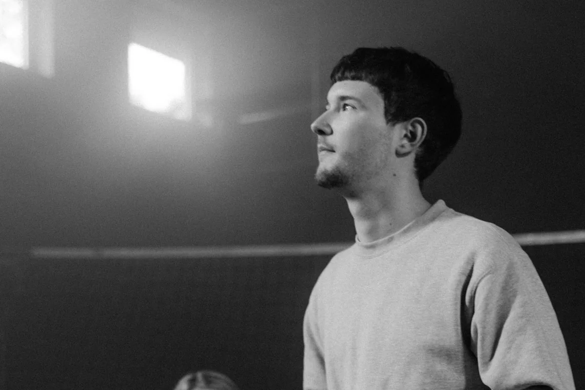 Exercise in the improv workshop Black and white: a young man in a light sweatshirt looking upwards, light falling through a tall window behind him